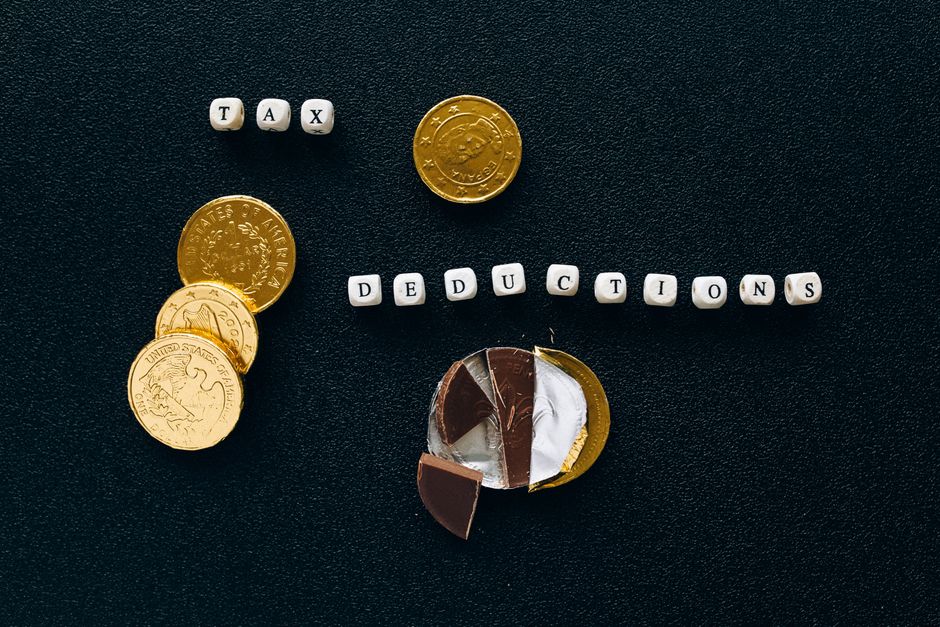 Creative concept of tax deductions using chocolate coins and letter tiles on a black background.