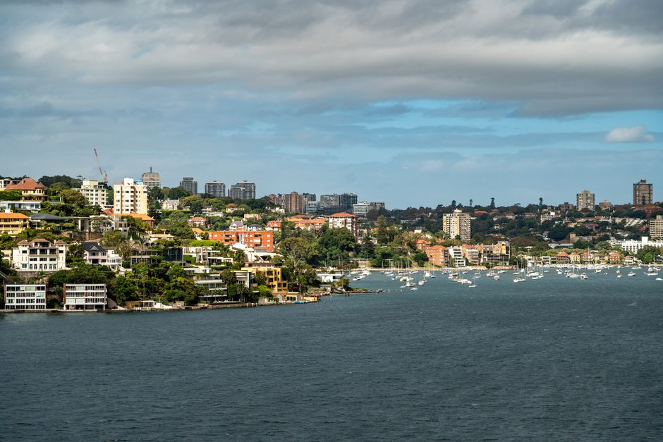 Scenic view of Sydney’s harbour with boats and waterfront residences under a cloudy sky.