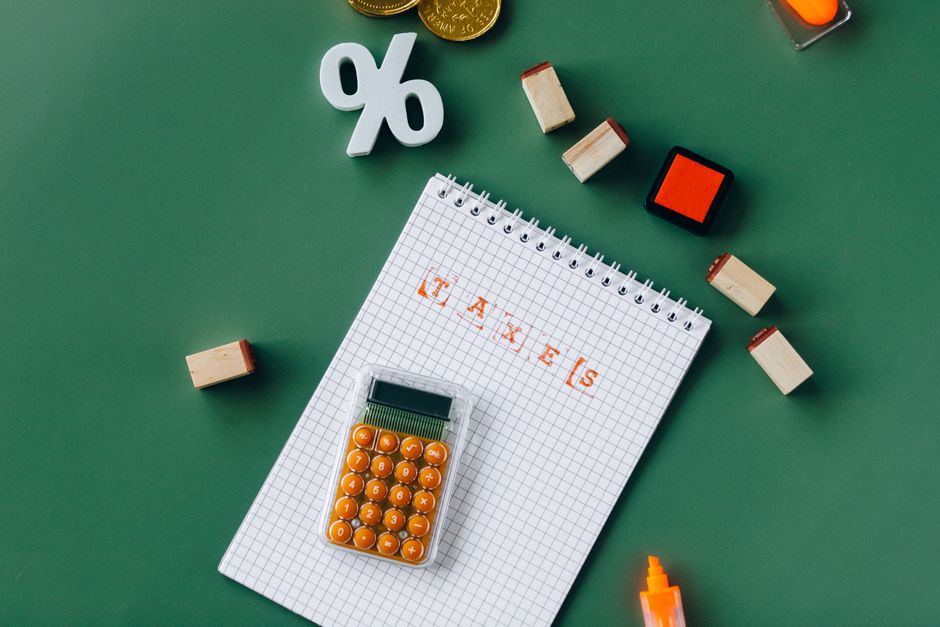 Flat lay of tax essentials with calculator, notebook, and stamps on a green background.